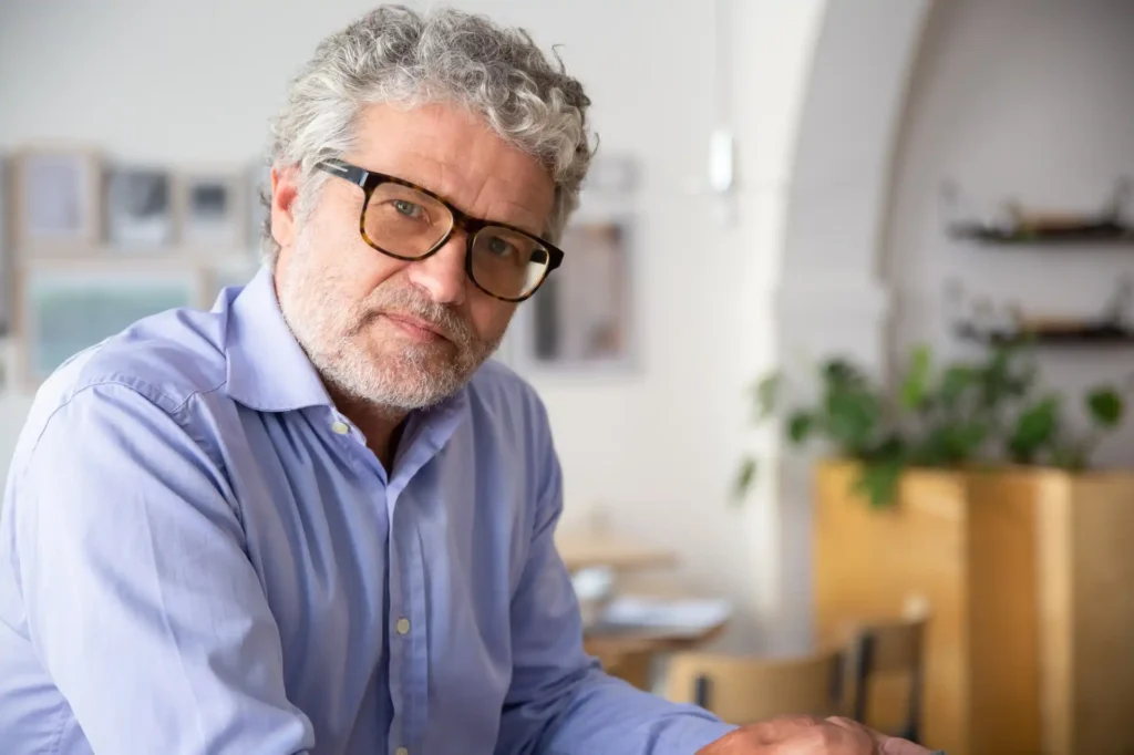 Professor de cabelos grisalhos e óculos escuros, sentado em escritório, representando dúvidas sobre precatórios Fundef