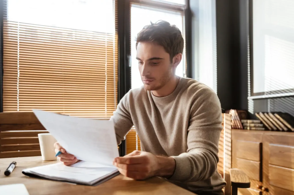 Homem estudando documentos relacionados a vender precatório em escritório moderno com iluminação natural